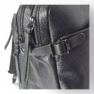 Close-up of a black leather bag showing a metal zipper and buckle with a pebbled texture.