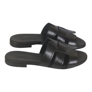 Black leather slide sandals with two overlapping straps, shown from a side angle.