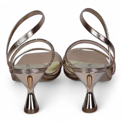 Pair of metallic rose-gold strappy high-heeled sandals viewed from the back, two-tone straps looping around the ankle and slim heels.