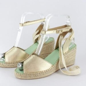 Gold metallic espadrille wedge sandals with ankle straps and green footbeds, displayed on a light background.