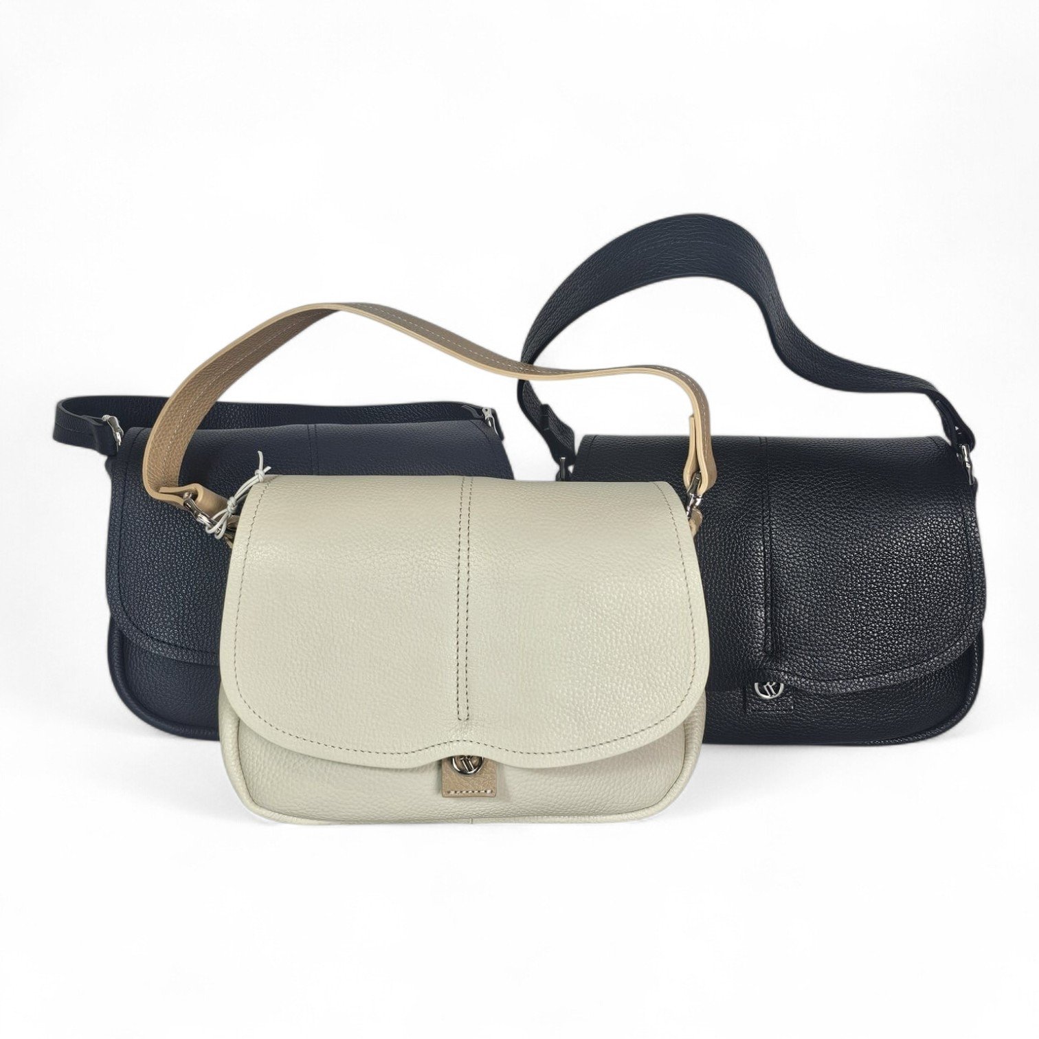 Beige front-crossbody bag with a curved flap, two dark navy bags behind it, all made of pebbled leather with straps showing.